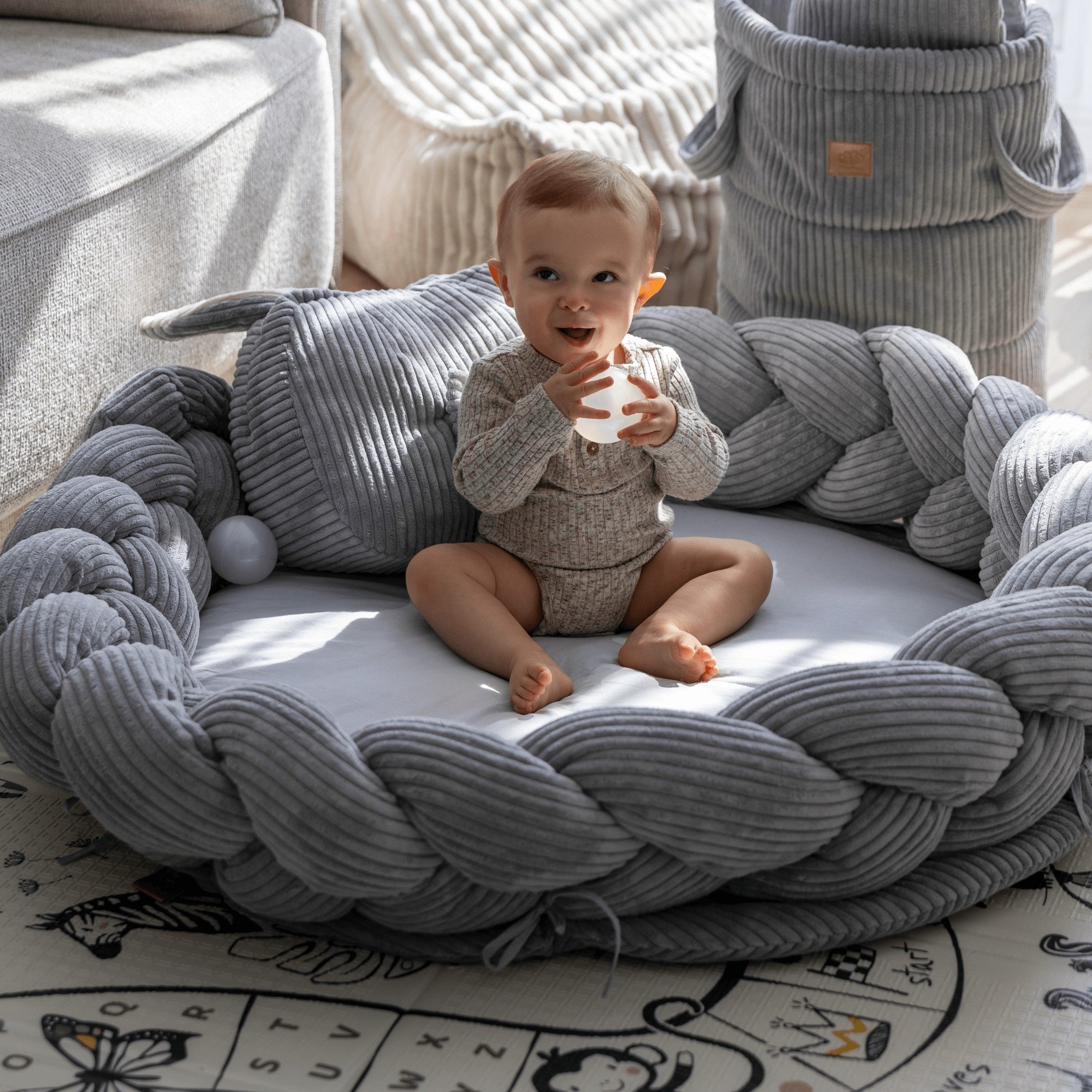 baby siting on grey playmat and drinks milk