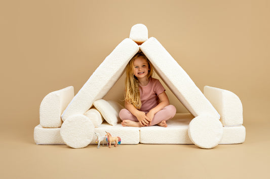 a little girl created a tent out of her white modular play sofa and is smiling