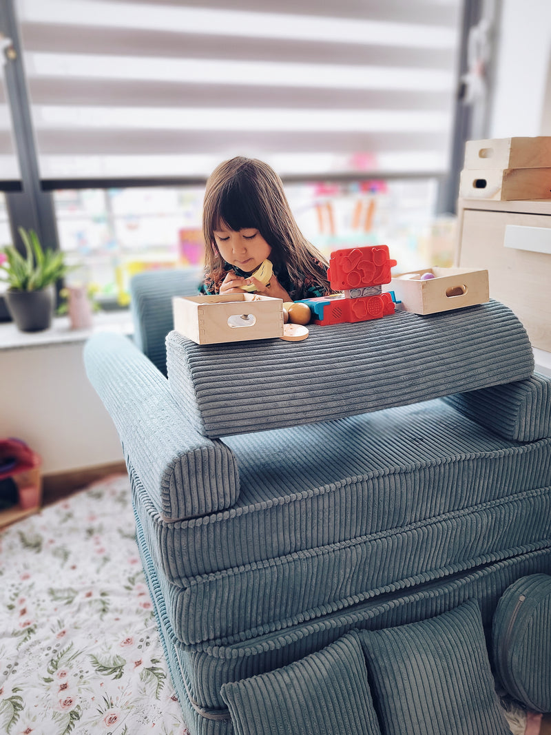 Child playing with toys on a blue couch in a room with plants and furniture.