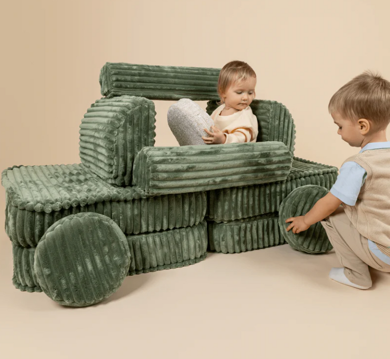 Two children playing with a green inflatable toy truck on a beige background