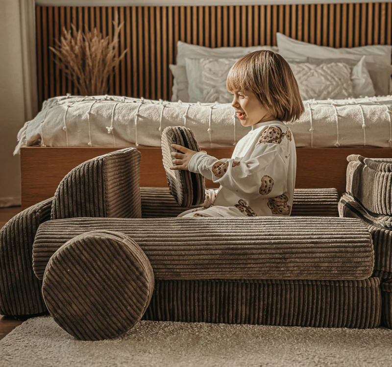 Child playing with a cardboard car in a bedroom setting