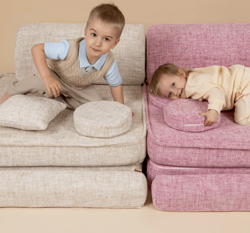 Two children on a beige and pink sofa with cushions.
