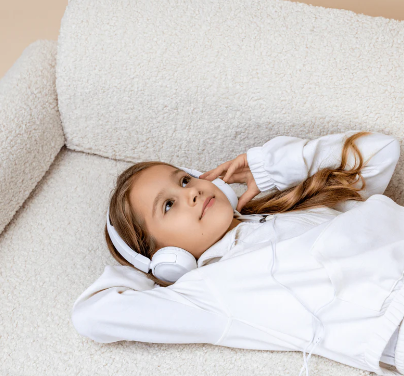 Young girl wearing headphones and lying on a beige sofa