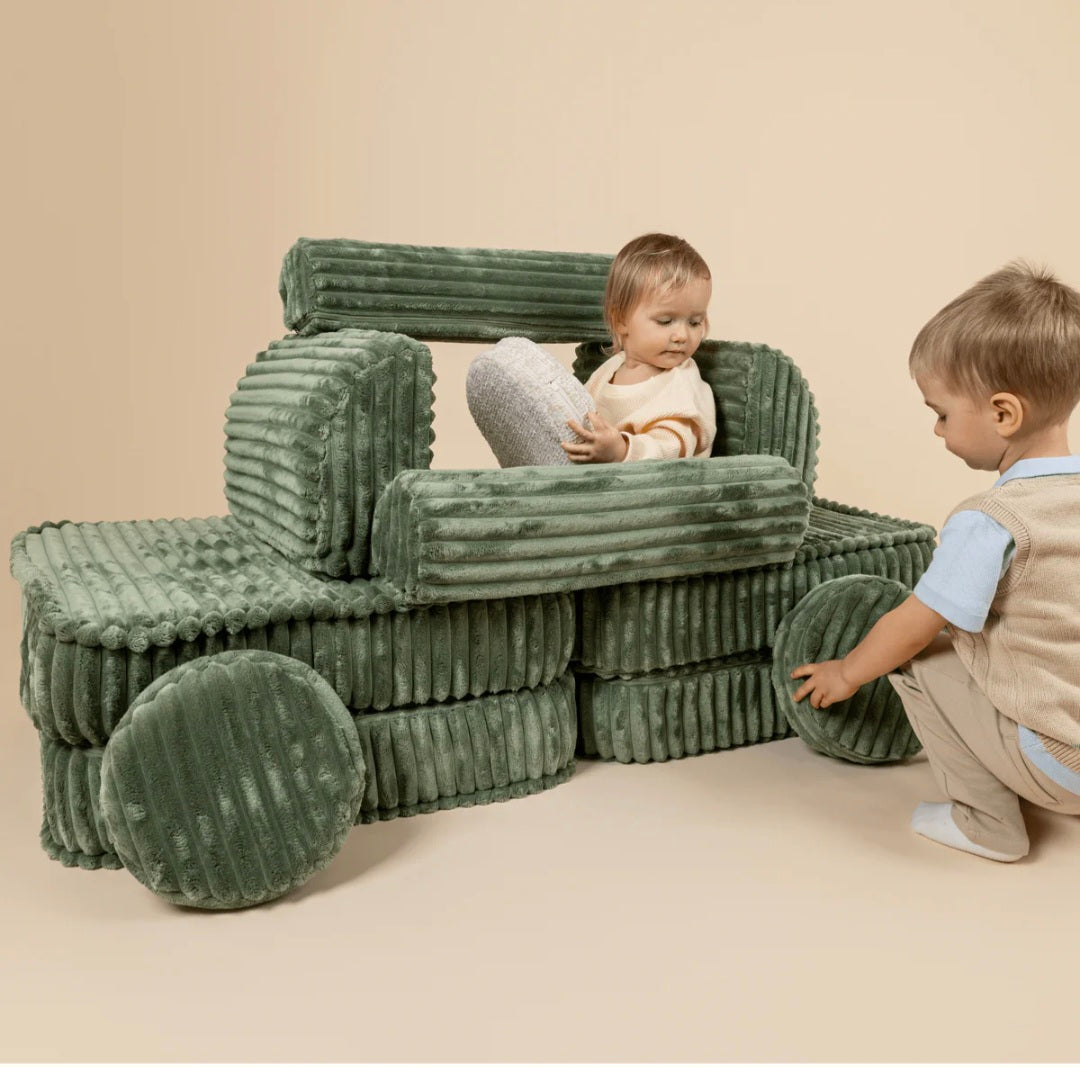 Two children playing with a green inflatable vehicle on a beige floor.